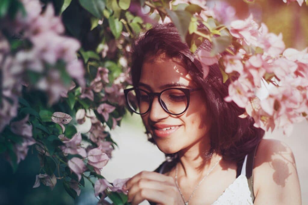 teen girl wearing eyeglasses standing in tree with pink flowers, picking petals and looking at peace